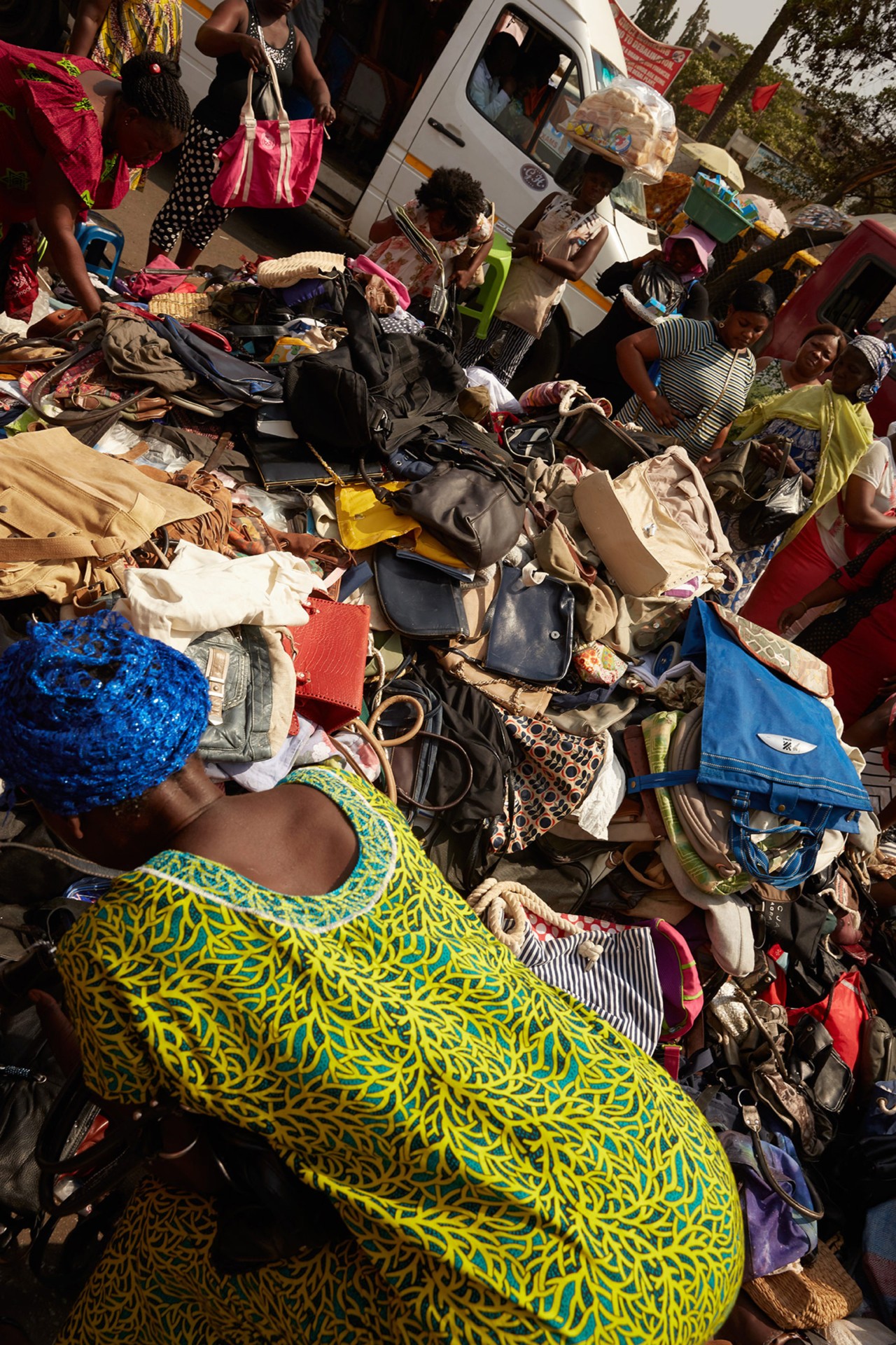 A woman in a green dress sorts through second hand handbags in Kantamanto market in Accra Ghana by Charlie Engman