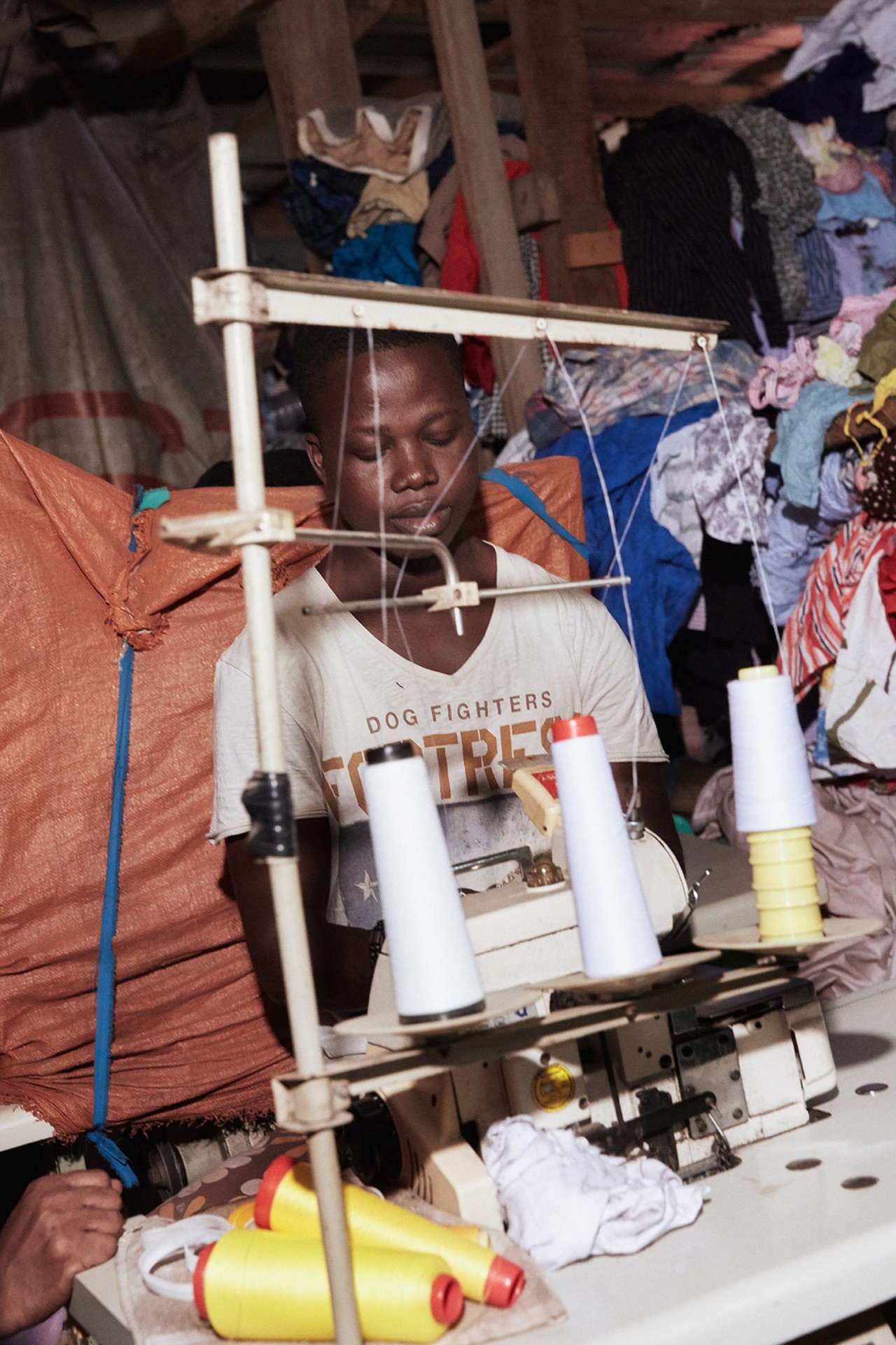 A young tailor repairs second hand clothing in Kantamanto Market in Accra Ghana by Charlie Engman