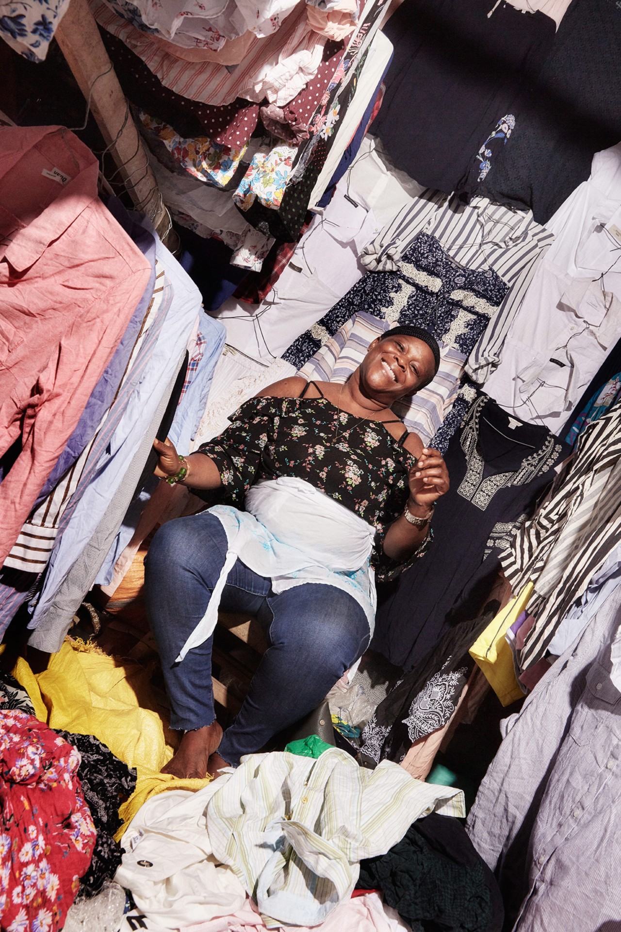 A retailer smiles in her stall in Kantamanto market in Accra Ghana by Charlie Engman