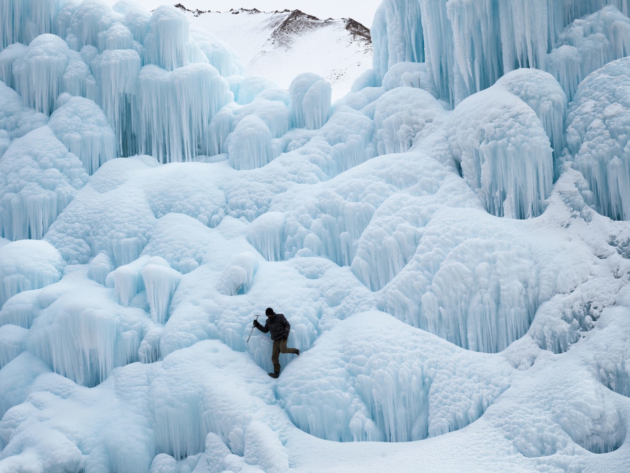 A person with an ice pick climbs an ice stupa in Ladakh India by Greg White