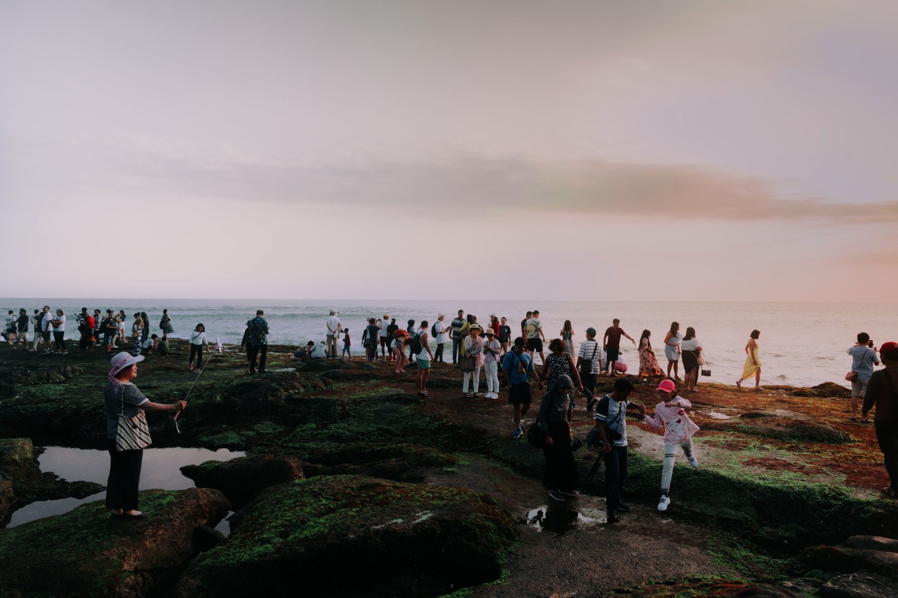 Tourists taking photos on rock at sunset in Bali Indonesia by Rishabh Malik