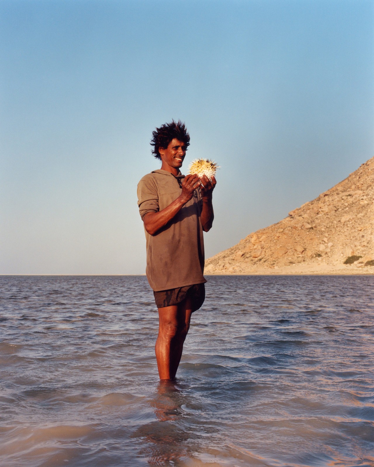 A man stands in the water and holds a blowfish in Socotra Yemen by Jamie Hawkesworth