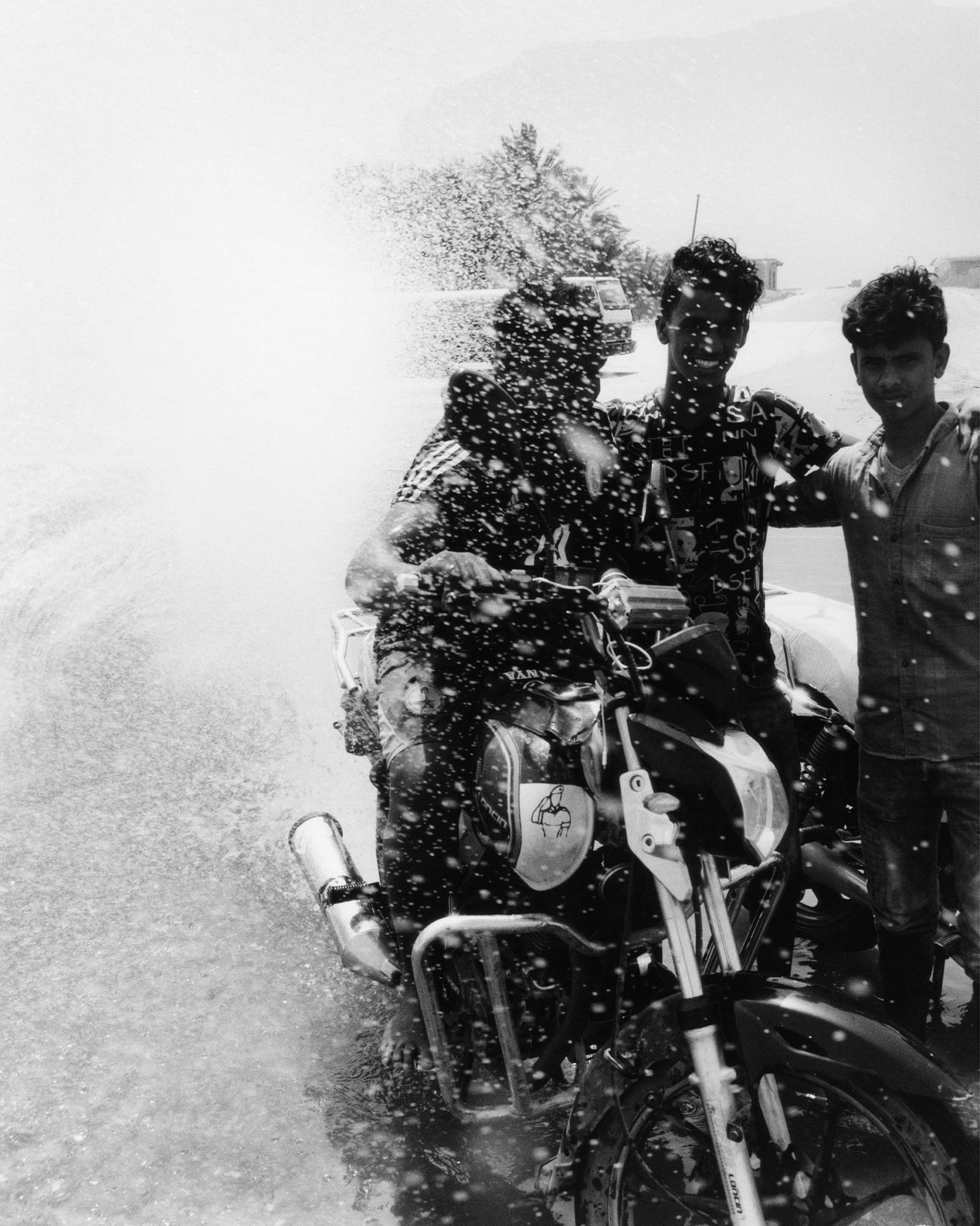 Three young men splashed by water as they ride a motorcycle in Socotra Yemen by Jamie Hawkesworth