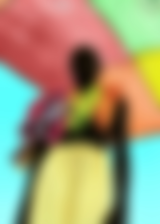 A boy wearing yellow shorts and several garments draped over his shoulders stands below a multi-colored roof.