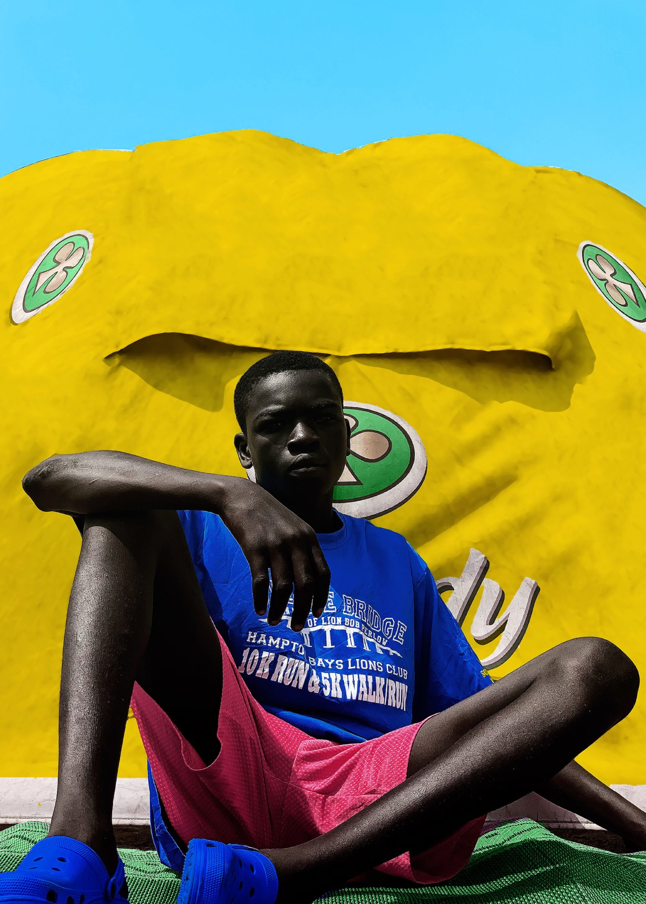 A boy in a blue shirt and red shorts sits on the ground.