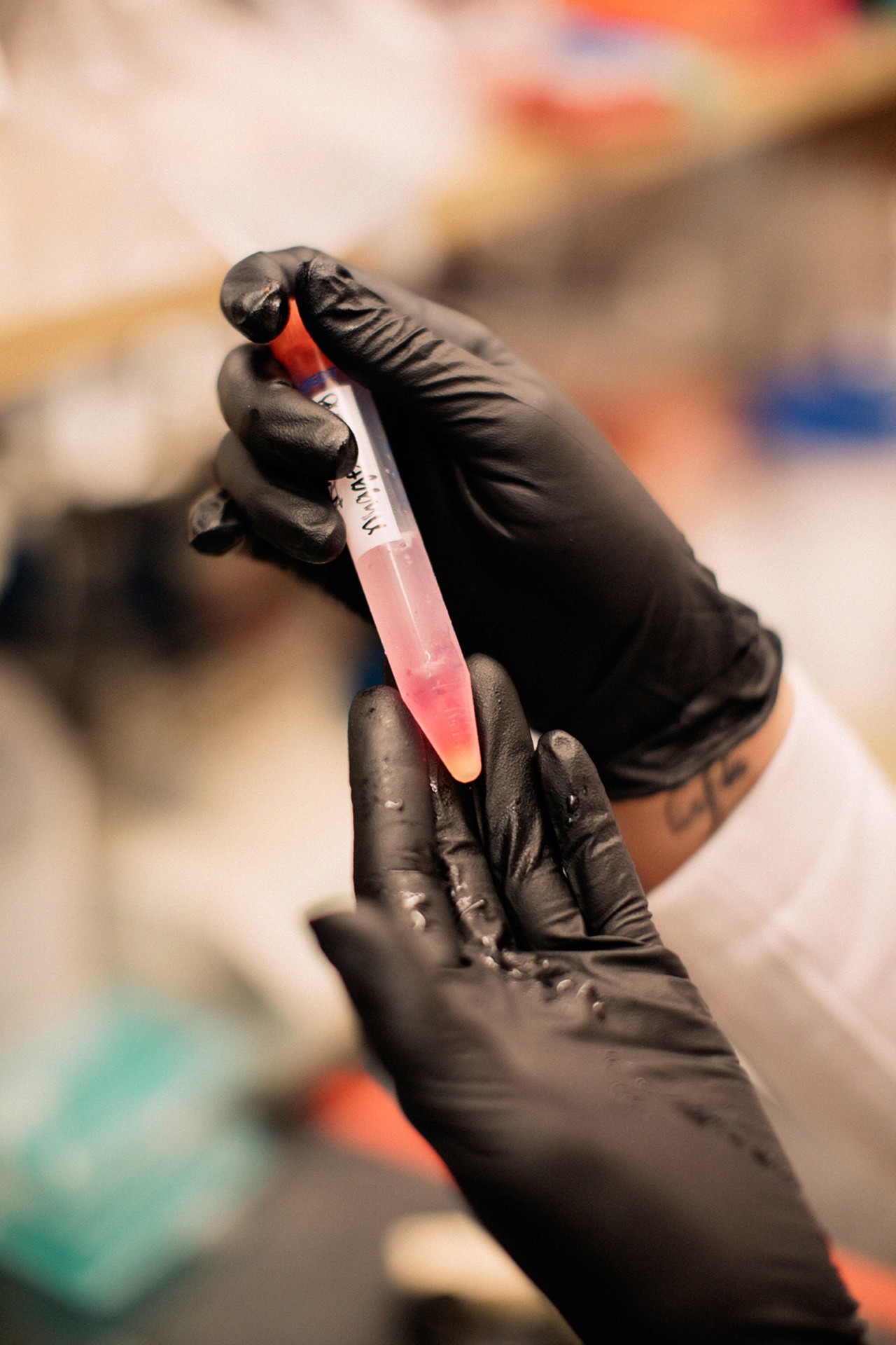 Black gloves holding test tube in lab by Rich Gilligan