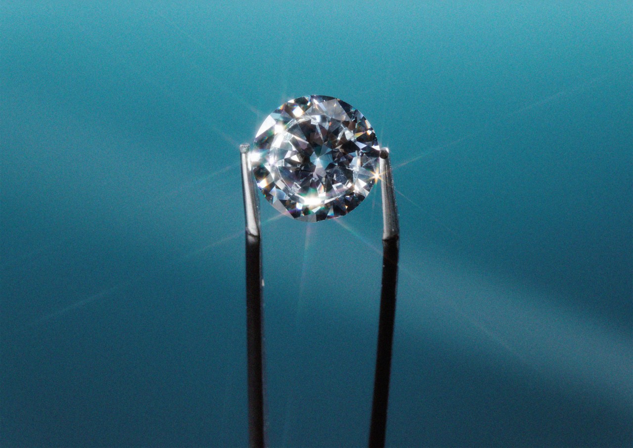 Tweezers holding diamond against blue background