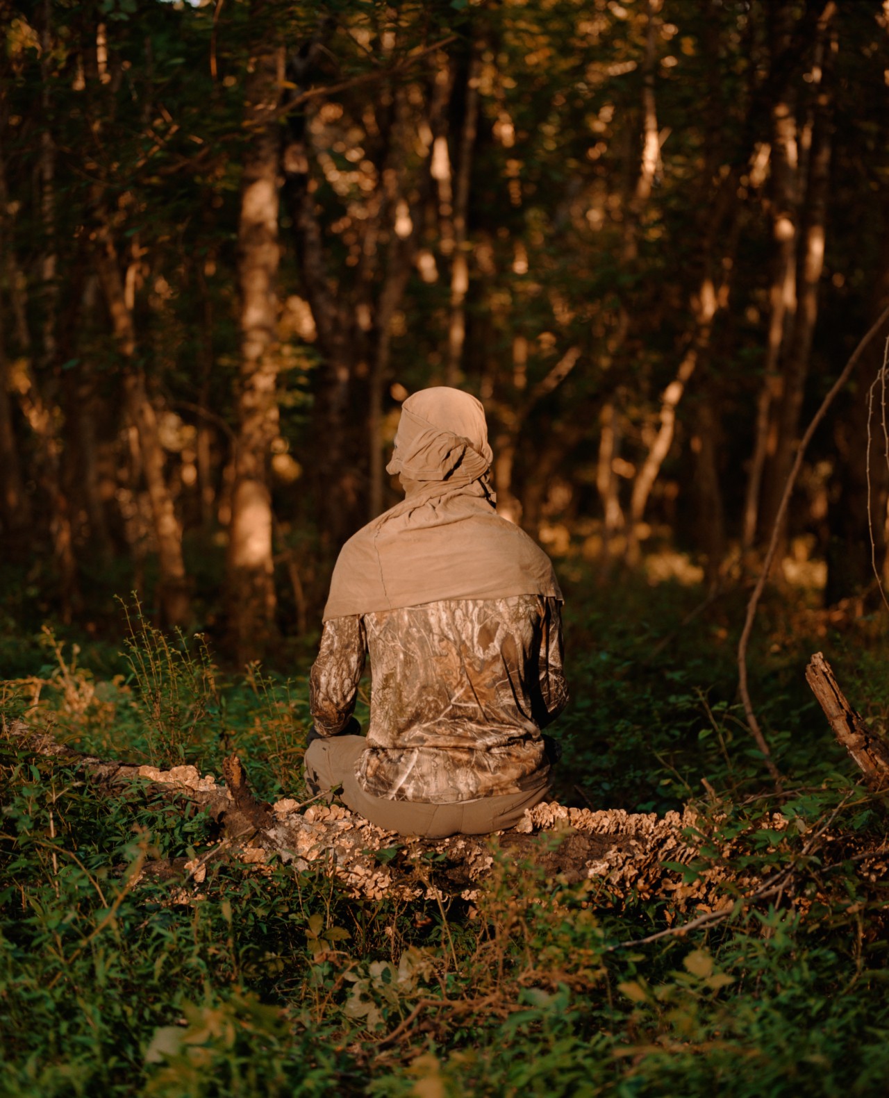 A forest defender dressed in camouflage sits on a log near their treehouse, which is the site of a protest occupation to defend the forest near Atlanta