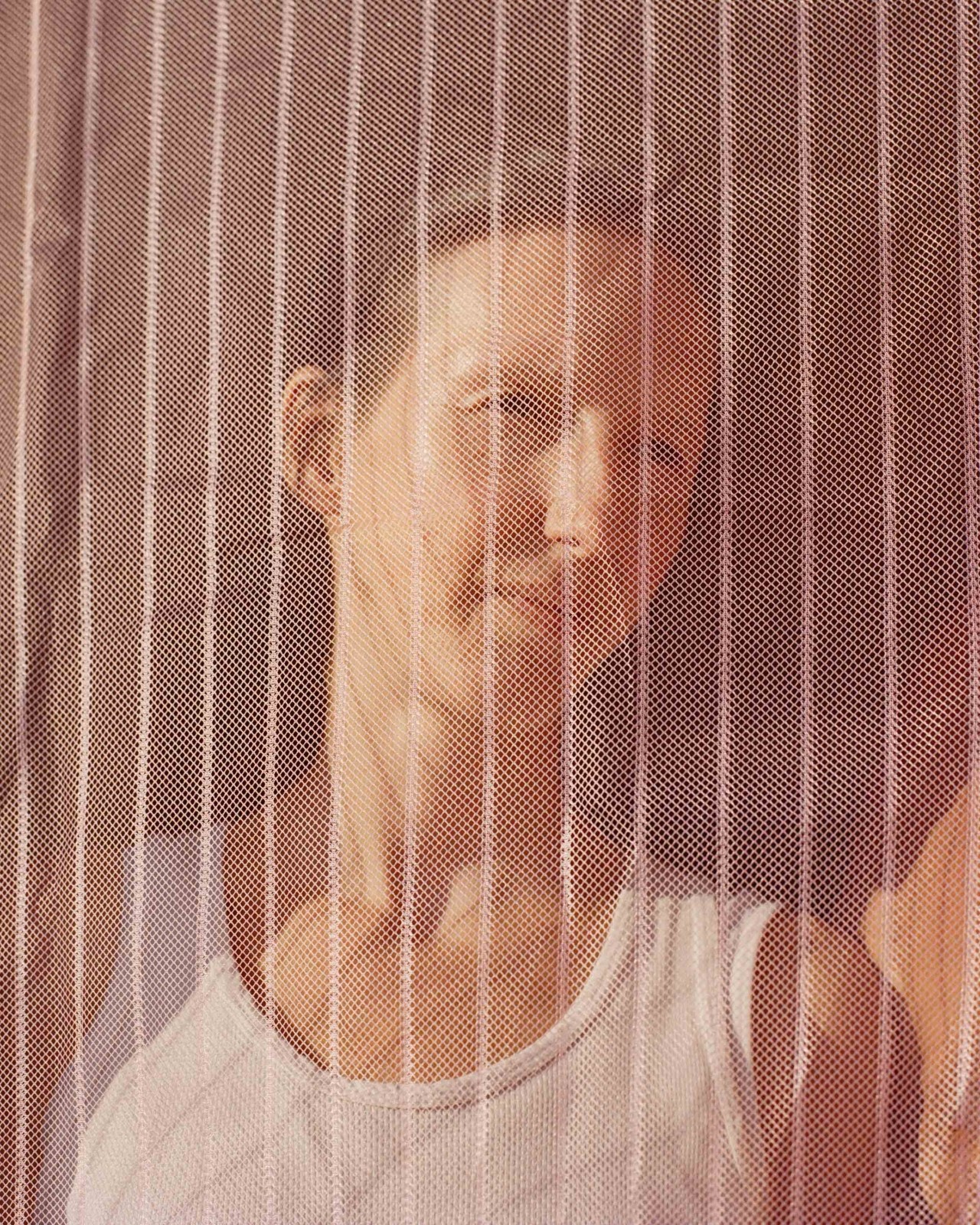 A woman faces the camera while looking in the distance through a sheer, pinkish net material.