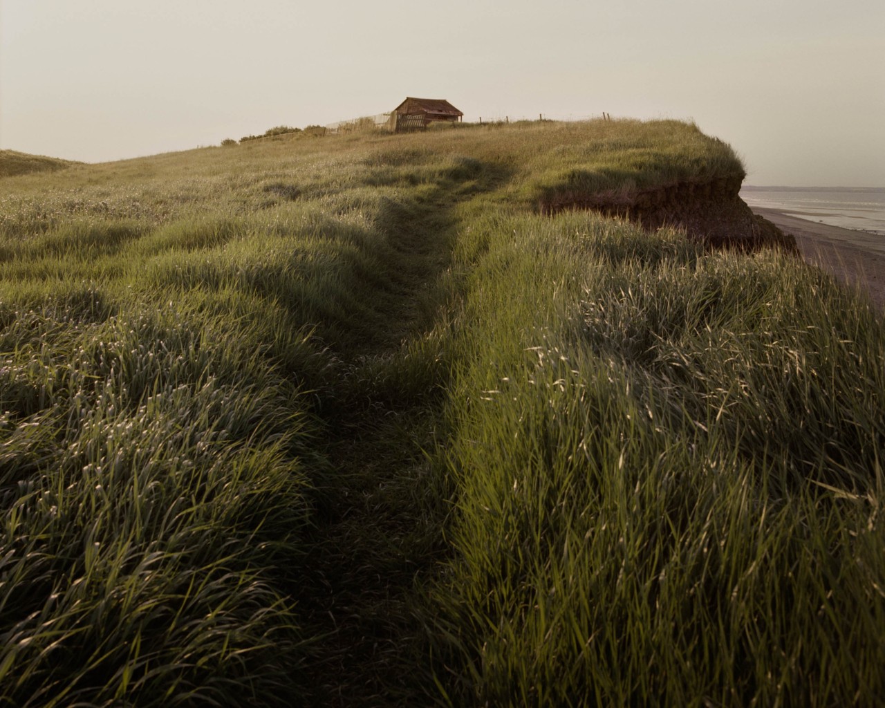 A house sits atop a grassy cliff overlooking the British coast.
