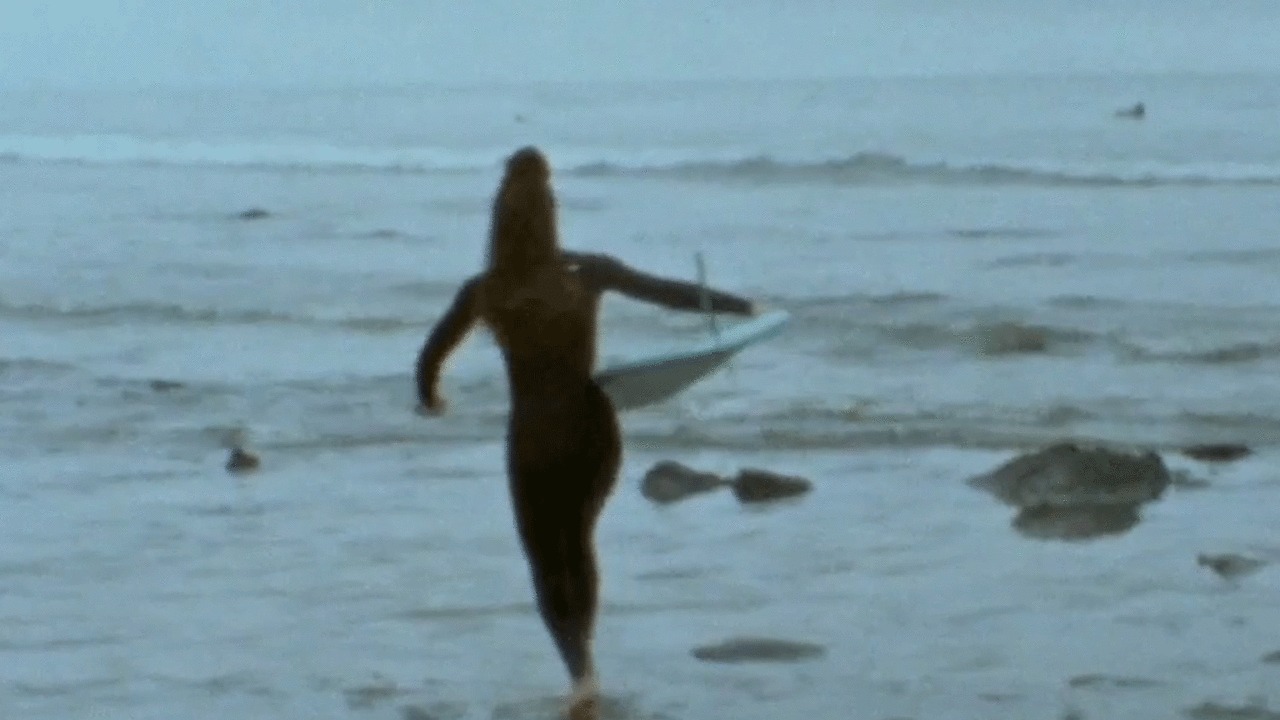 Kimiko Russell-Halterman, Brown Girl Surf educator runs toward ocean while carrying a surfboard. She is facing away from the camera.