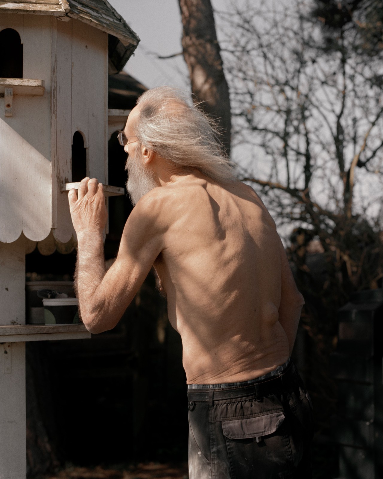 An older man peers inside a large white wooden mailbox with forest in background.
