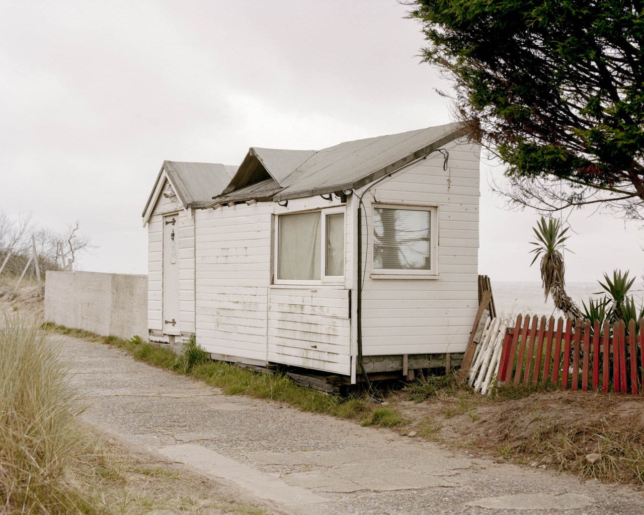 A small, white house sits between a narrow road and the British coast.