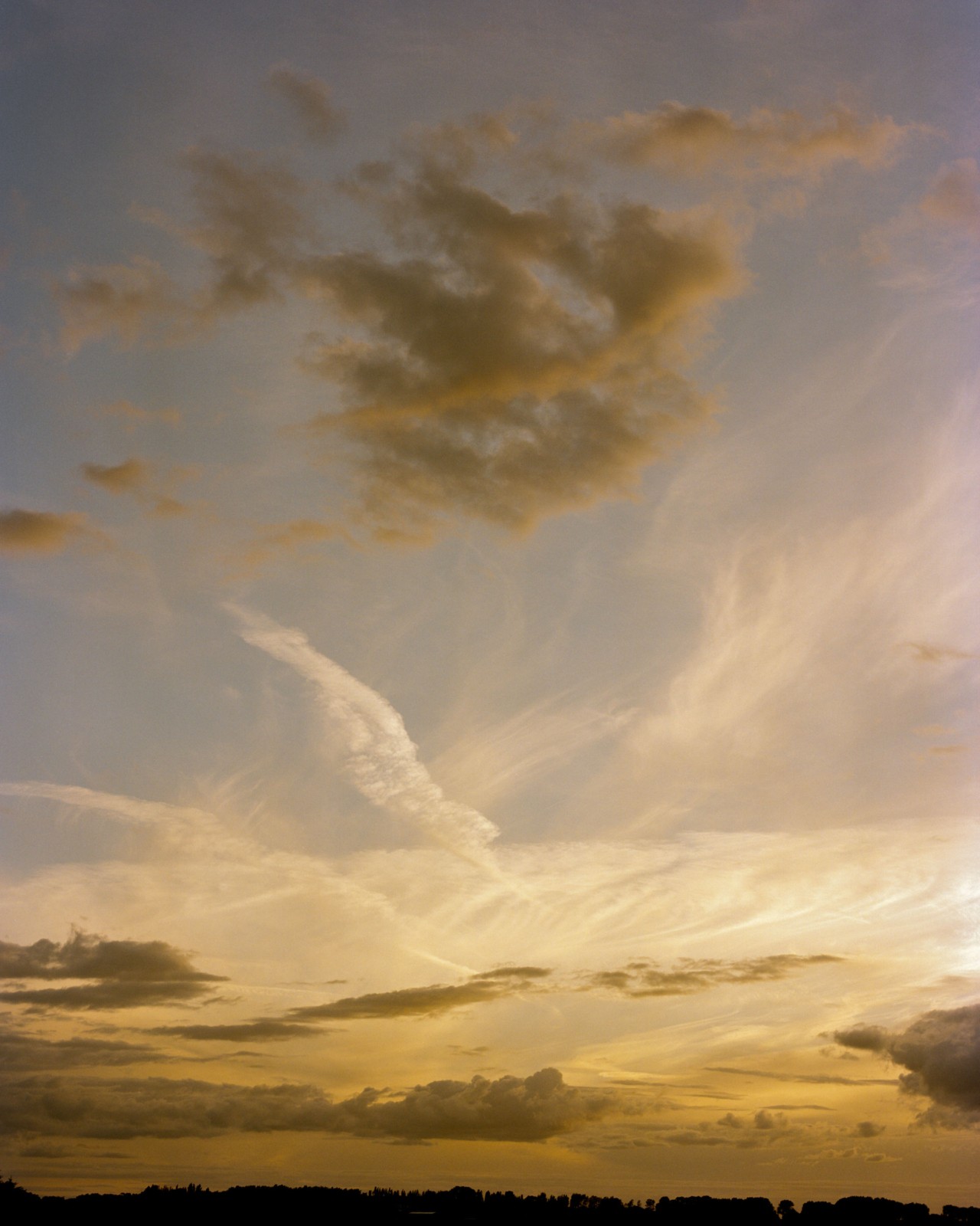 Several cirrus clouds are still in a blueish, yellow sunset sky.