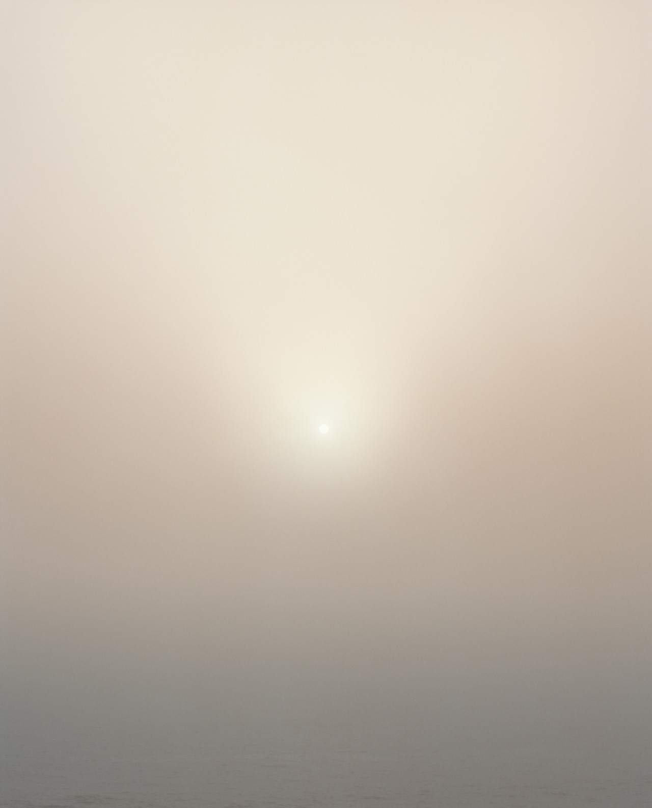 In the center of a smoggy sky sits a minuscule, bright sun in the far distance.