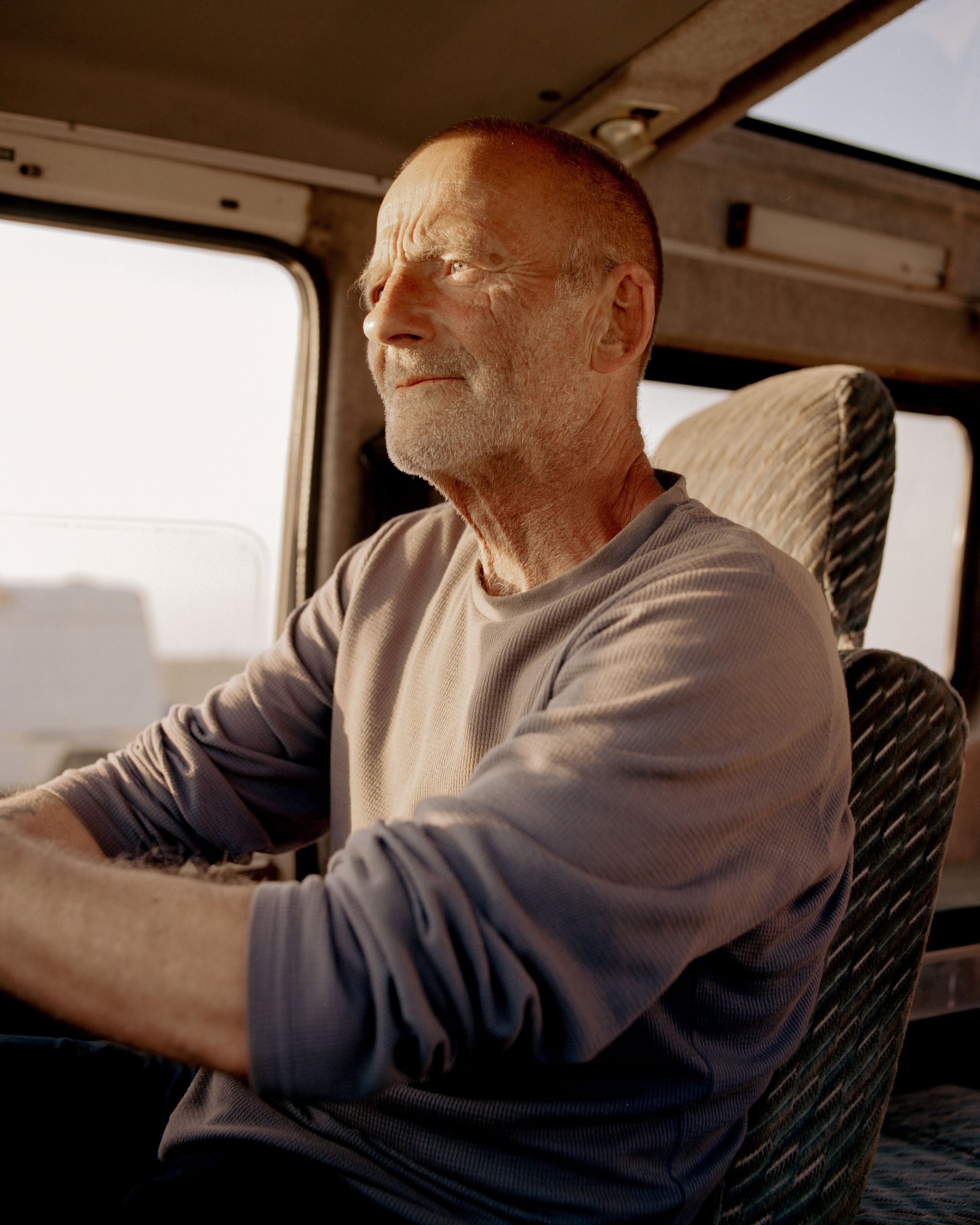 An older man looks straight ahead while driving along British coast.
