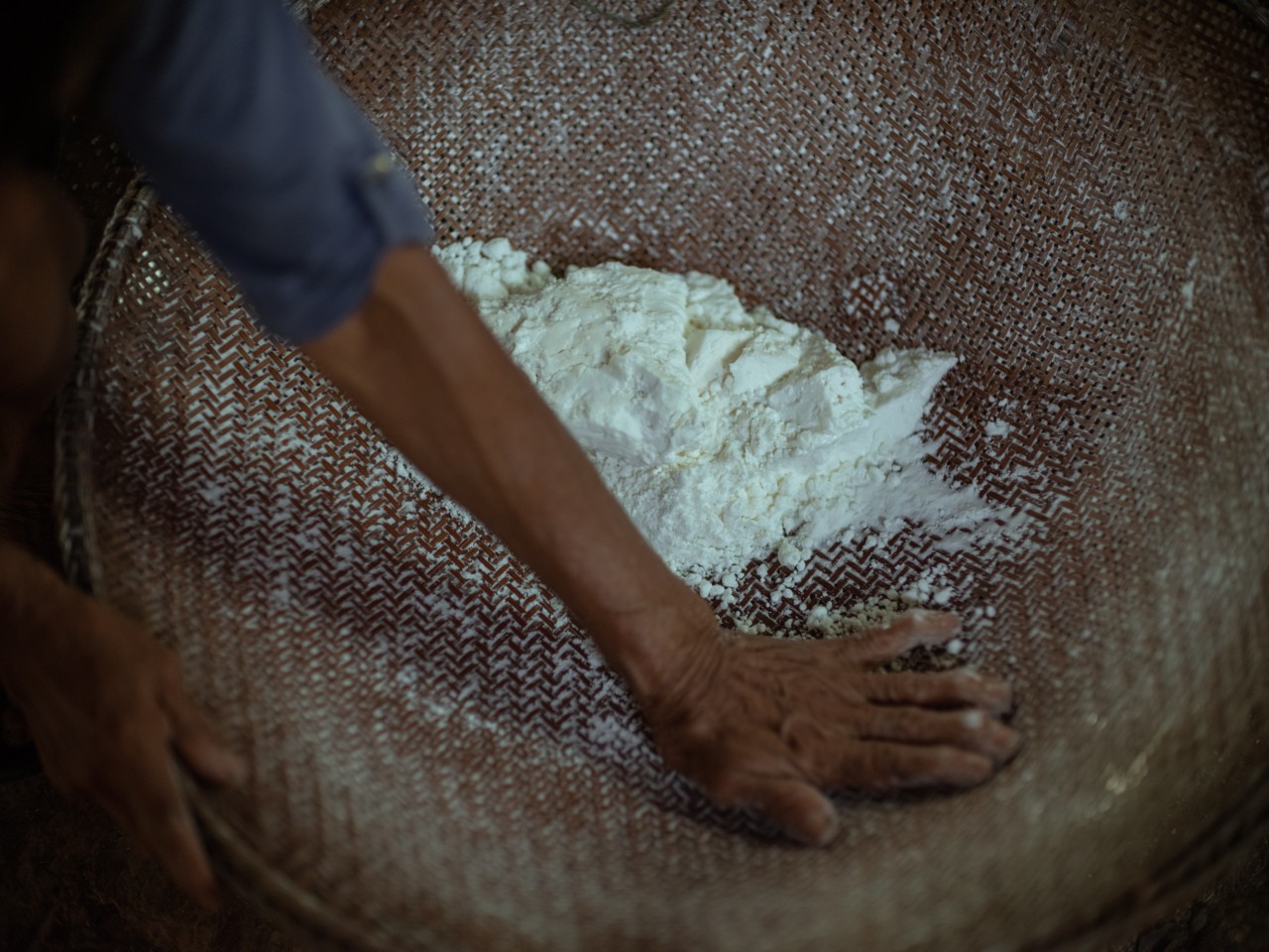 The arm of a person is shown reaching into a large basket filled with white powder.