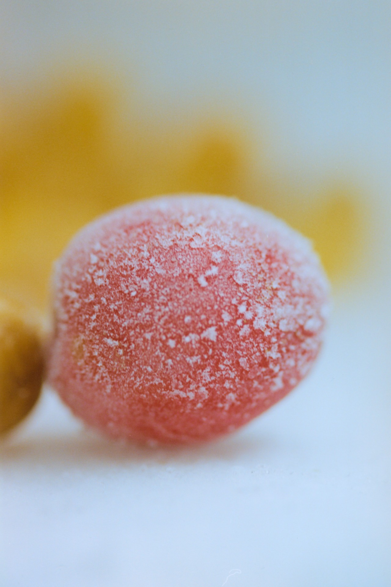 A small round food item that is pink and covered with a white crystalized substance.