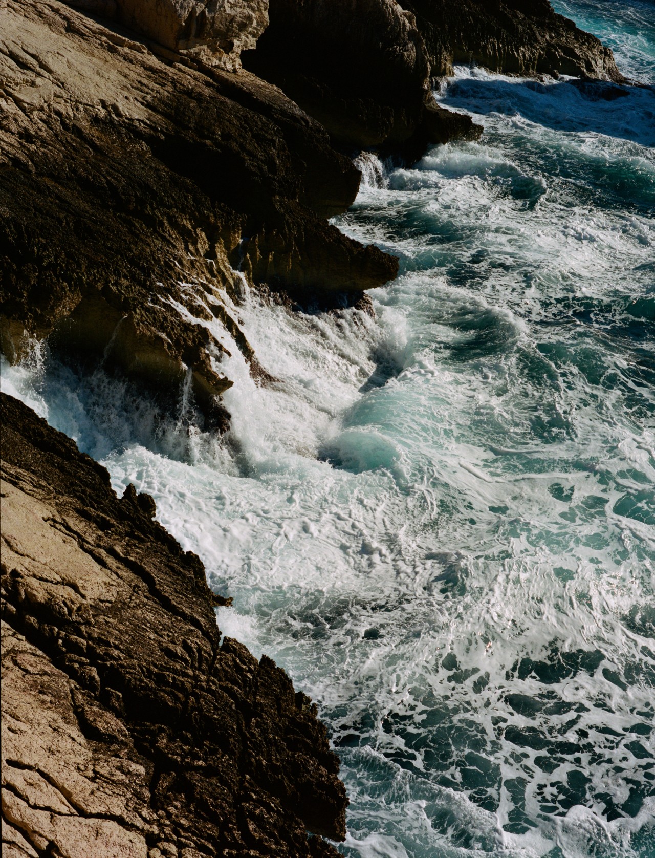 The ocean crashes into the rocky mountainous coastline.