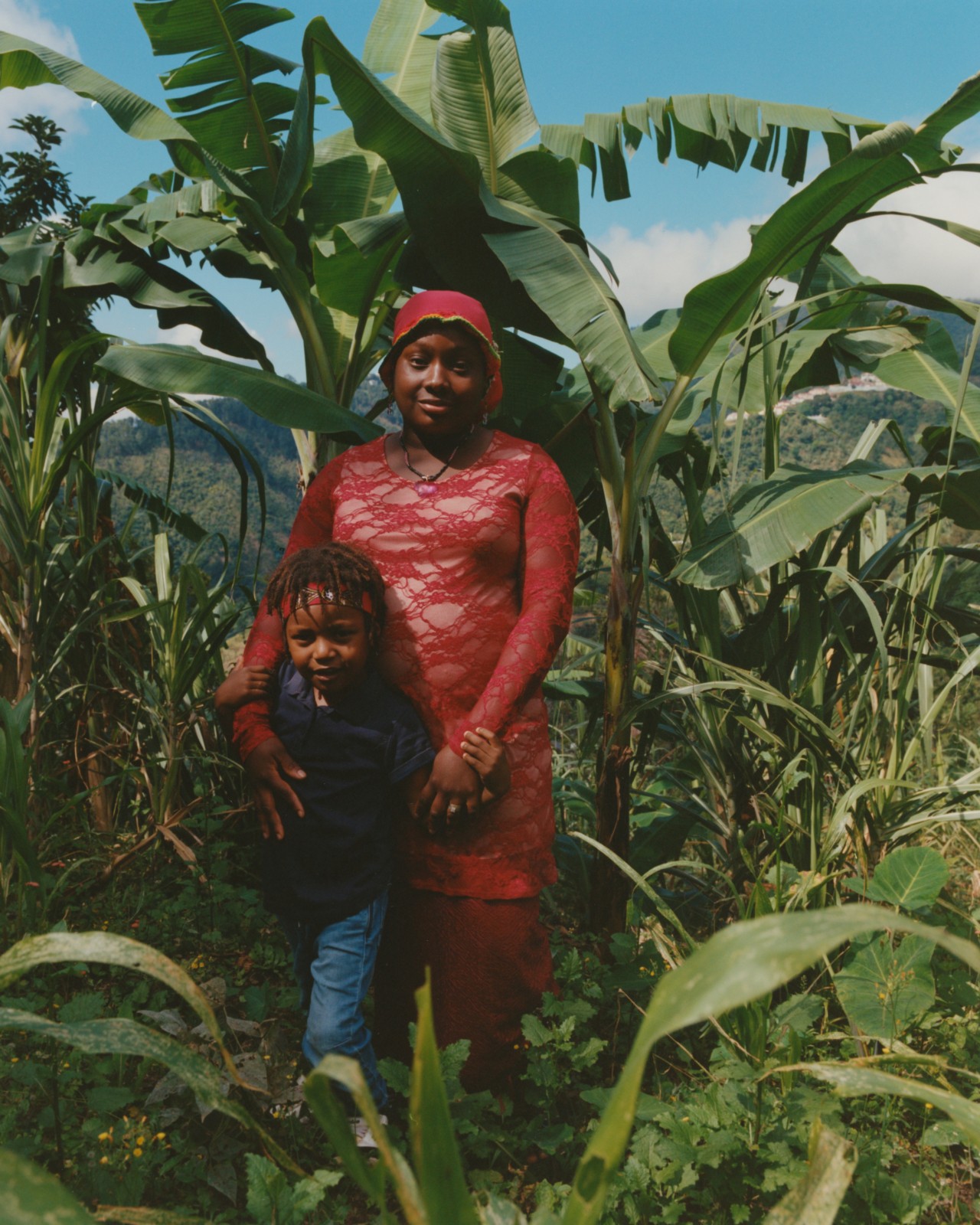 A Jamaican woman and a young buy stand next to each other amidst the jungles of Jamaica.