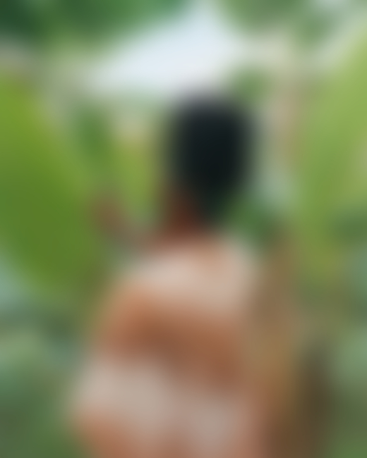 A Jamaican woman faces away from the camera as she grazes a large plant in jungles of Jamaica.
