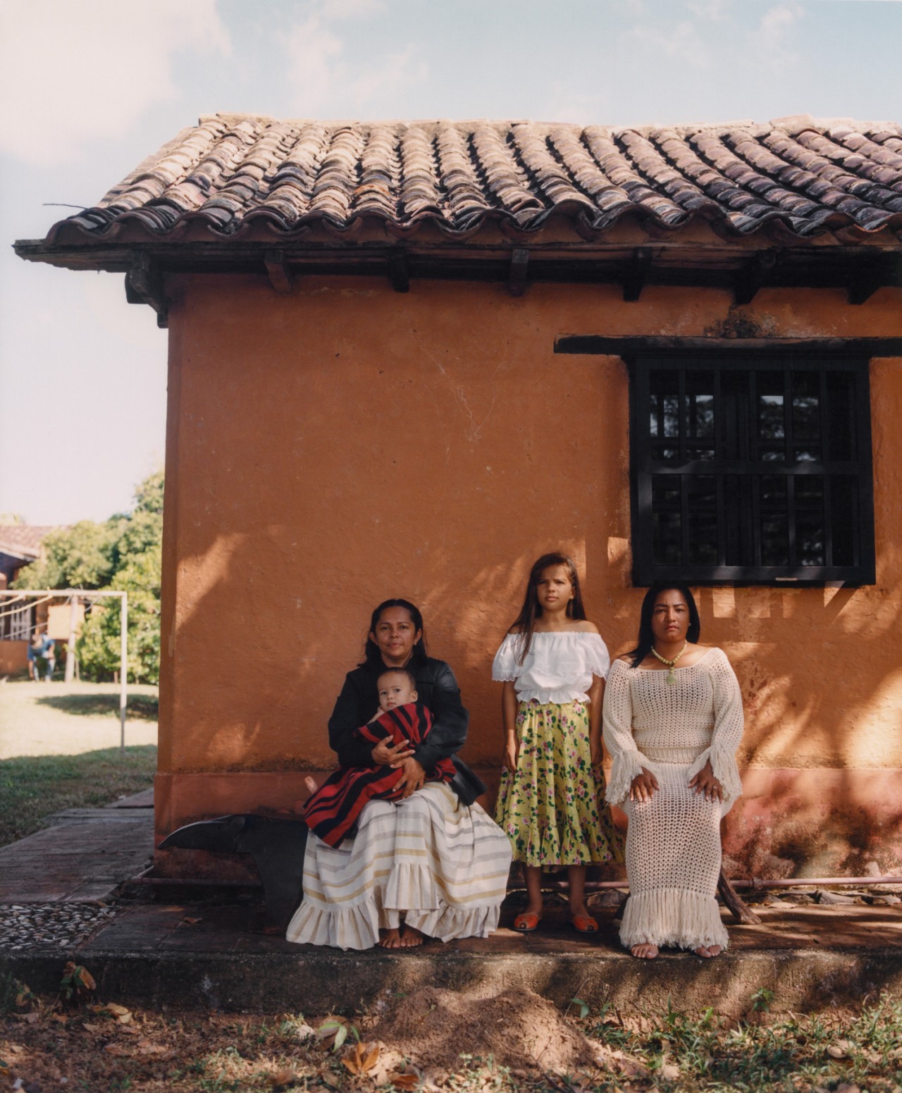 Two Venezuelan women, a child, and a baby are in front of a colorful home in Venezuela.