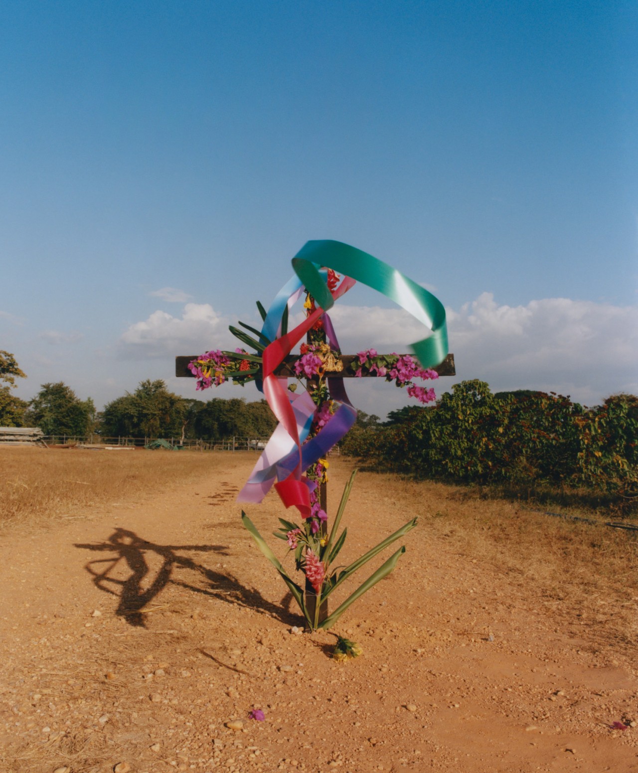 A large cross adorned in flowers and colorful ribbons blowing in the wind, sits amid the plains of Venezuela.