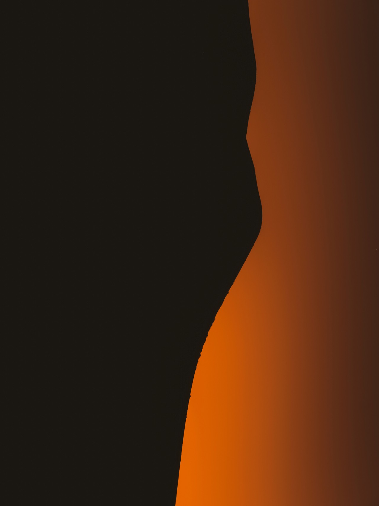 The sun sets along the horizon, behind a shadowed mountain