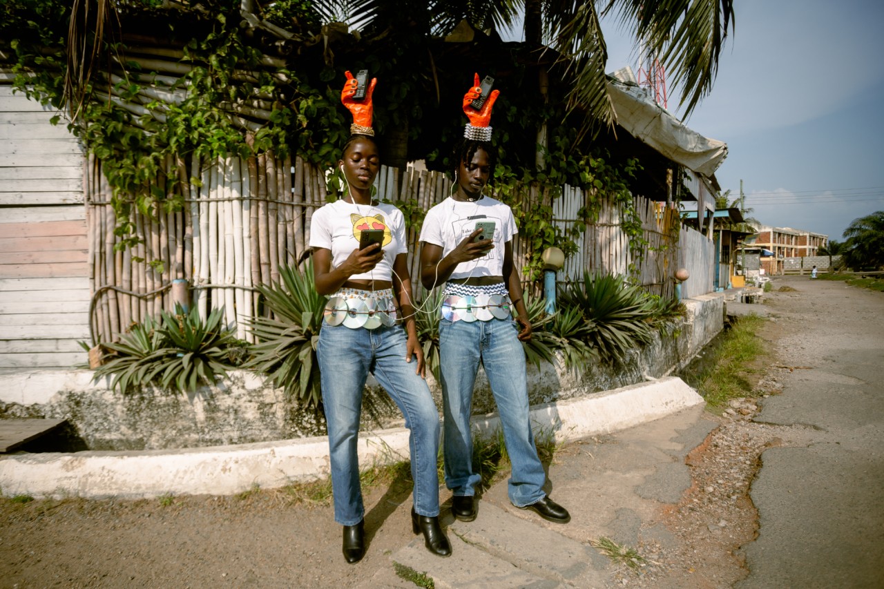 Two young people with matching clothes stand side by side while looking at their phones