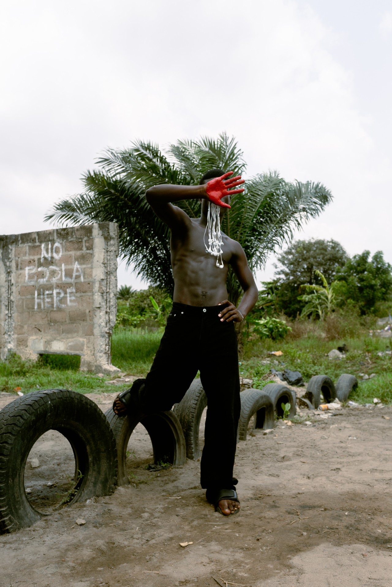 A man covers his face with a red painted hand while holding one leg on a tire