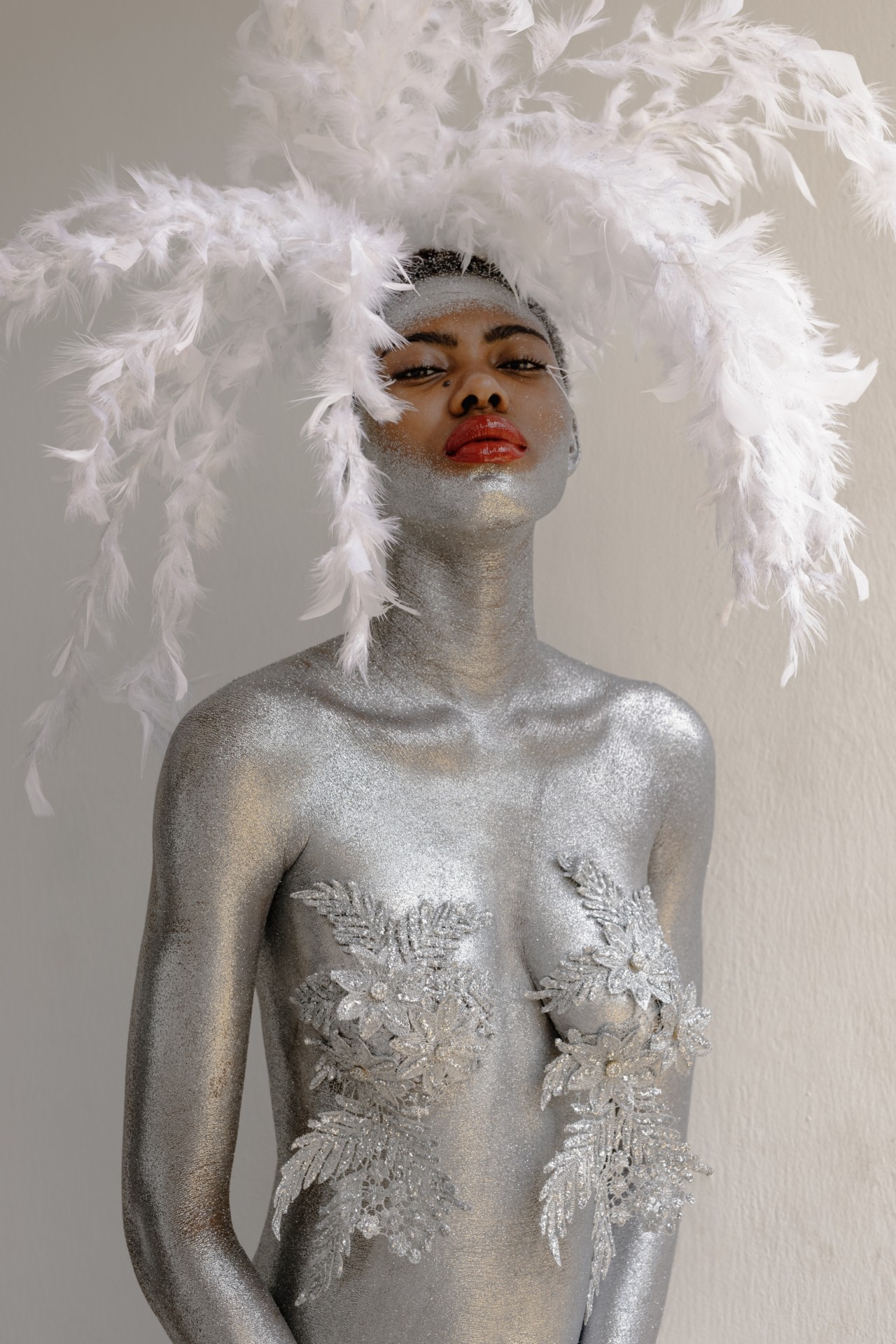 A carnival performer is covered in silver body paint and wearing feathers on top of her head.