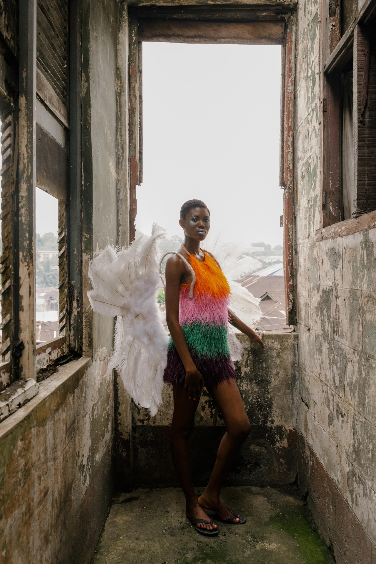 A carnival performer poses in an orange, pink, and green dress with large feathery wings.