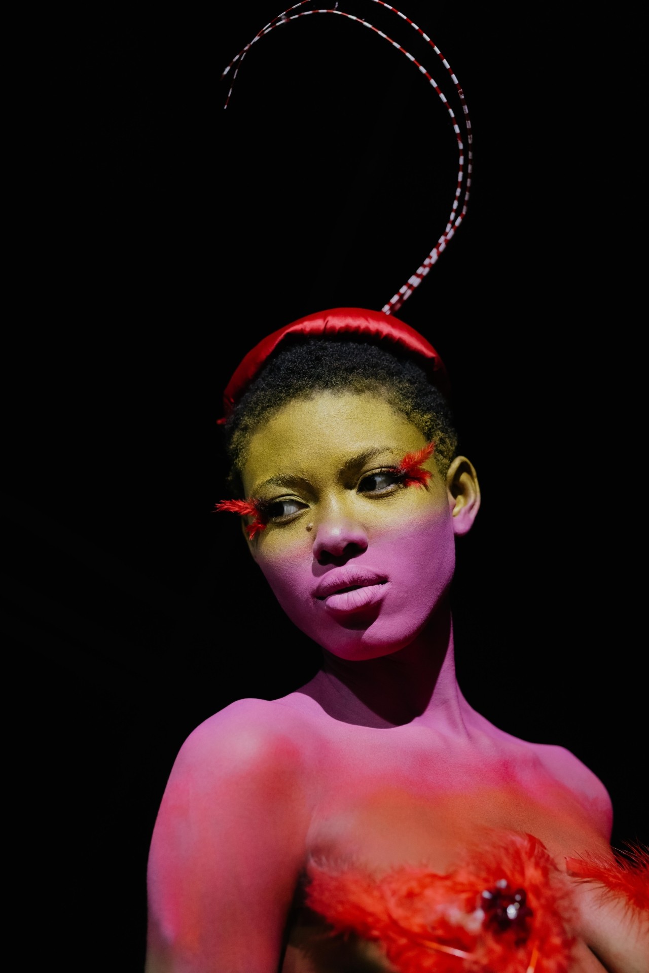 A carnival performer in yellow, purple, and red body paint poses.