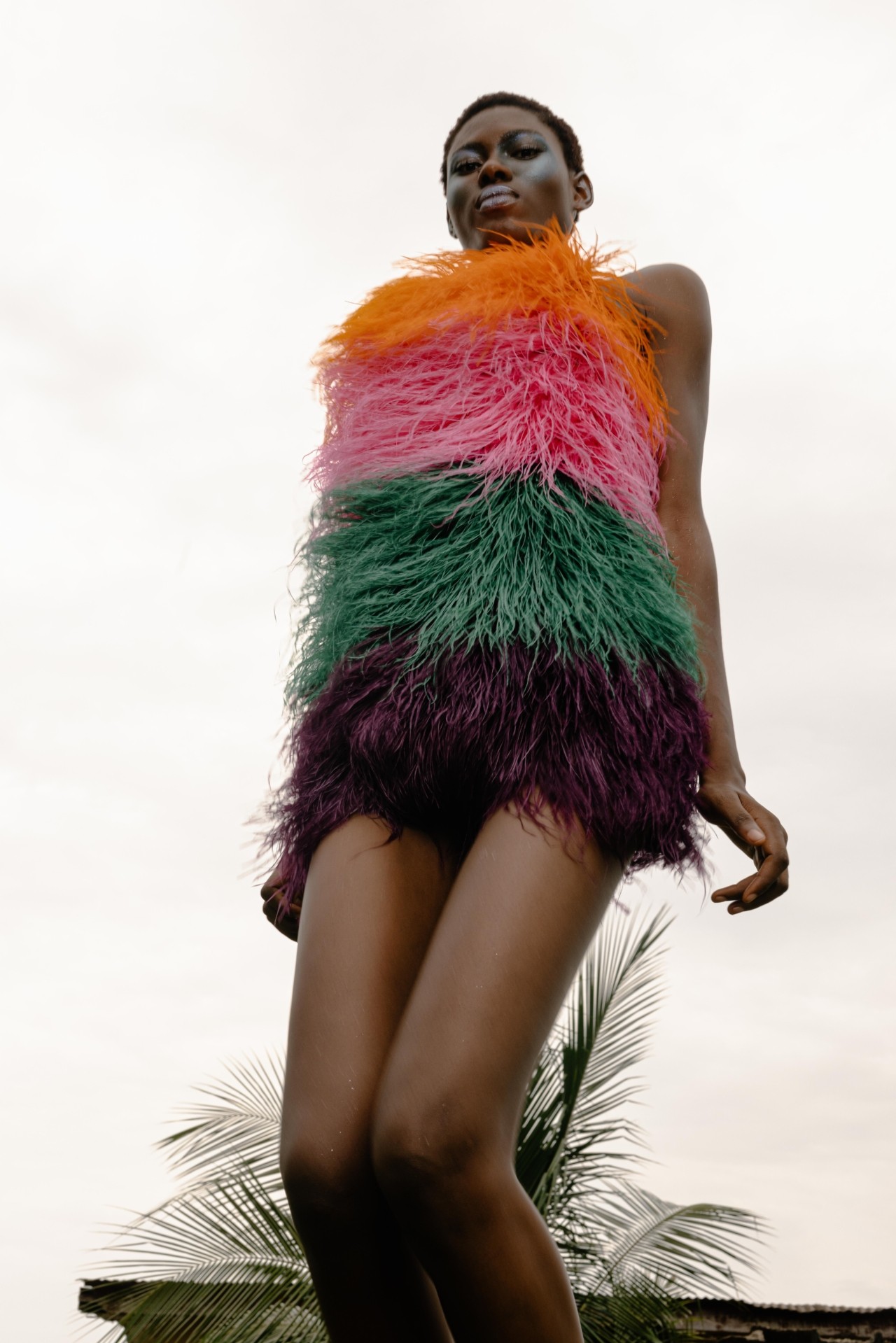 A woman dressed in a frilly colorful dress looks down at the camera.