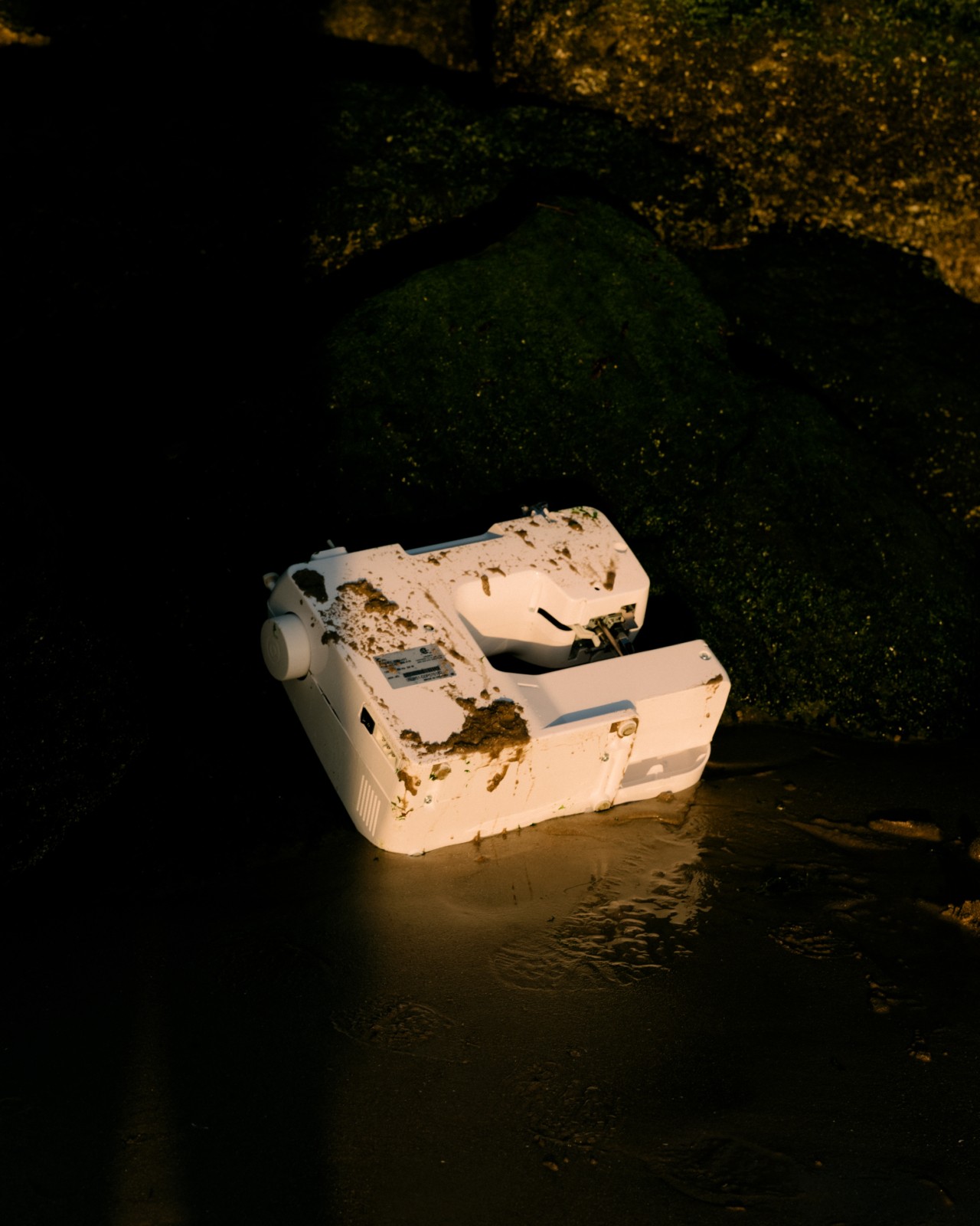 An abandoned, dirty sewing machine lies in the mud at the Rana Plaza site