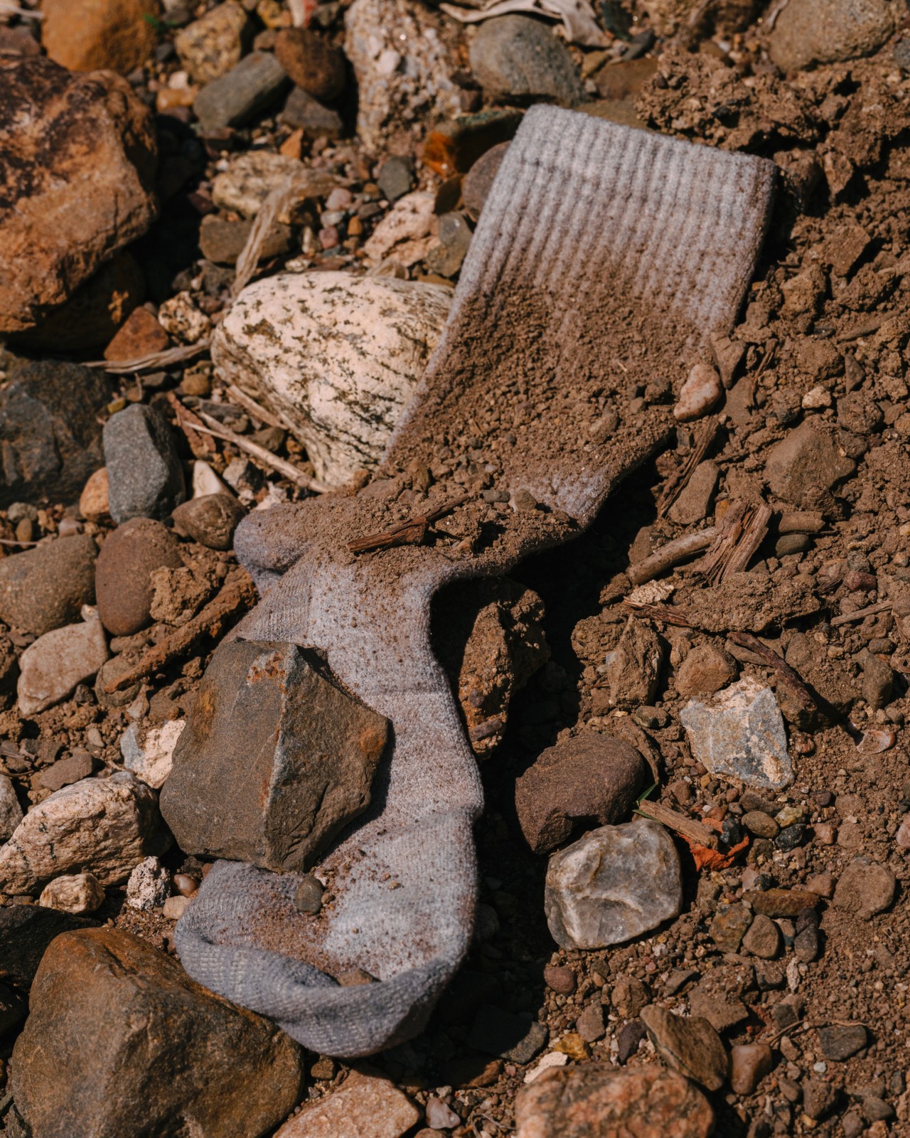 A blue sock is covered in dirt, rocks and rubble