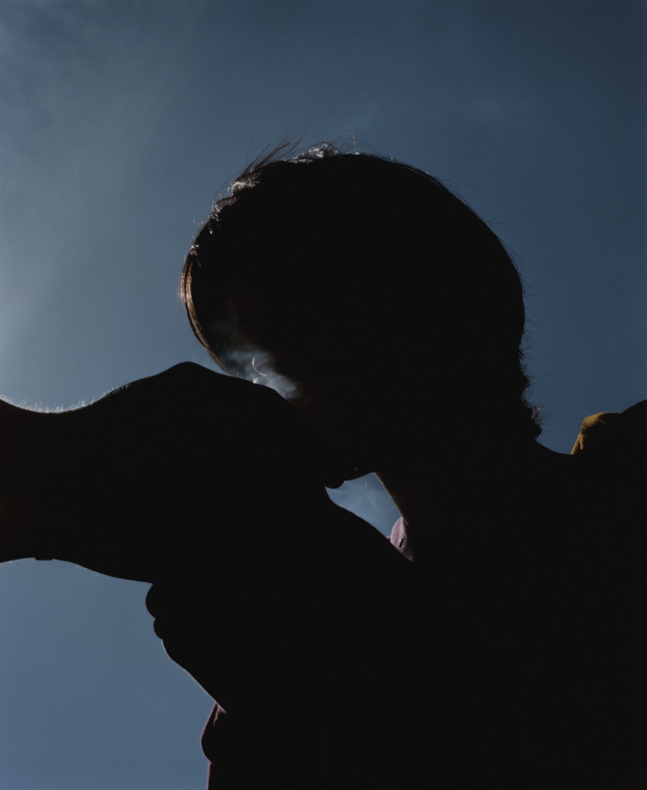 Silhouette of a teenager lighting a joint from below