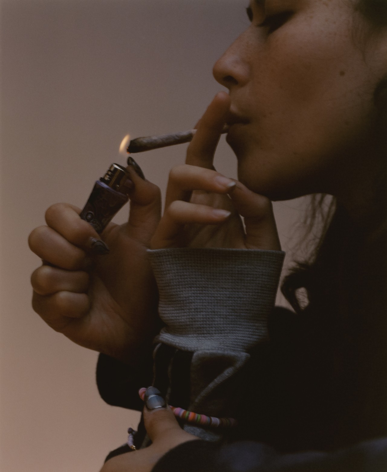 The side profile of a teen's face shown lighting a blunt and smoking it