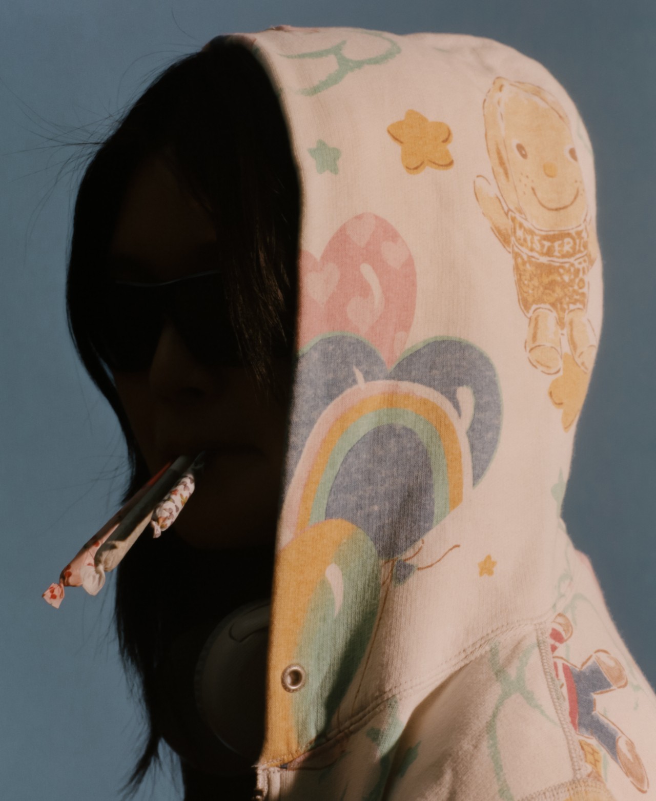 A teenager wearing a colorful hoodie balances three rolled blunts in their mouth