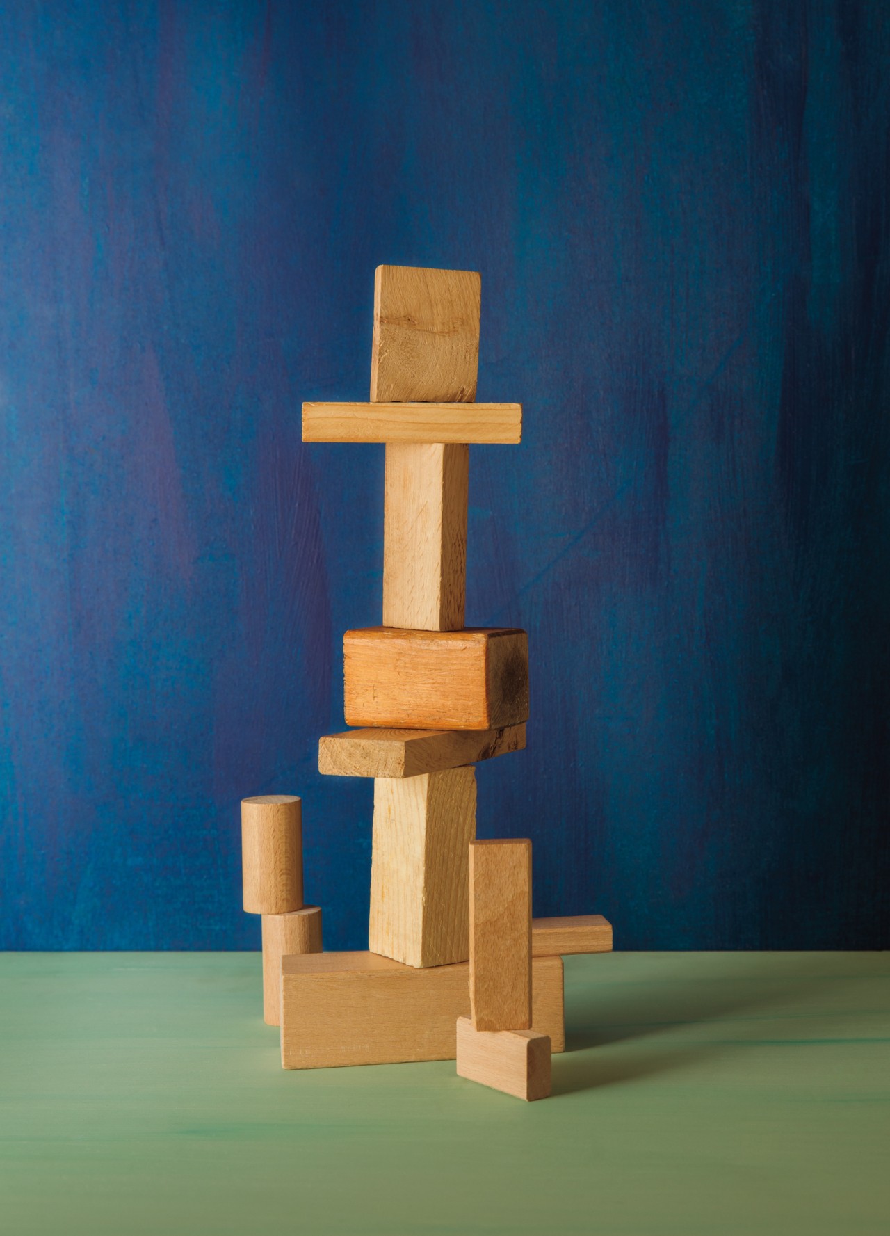 A bunch of small wooden blocks are variably stacked on one another on top of a green table. The back wall is painted blue.