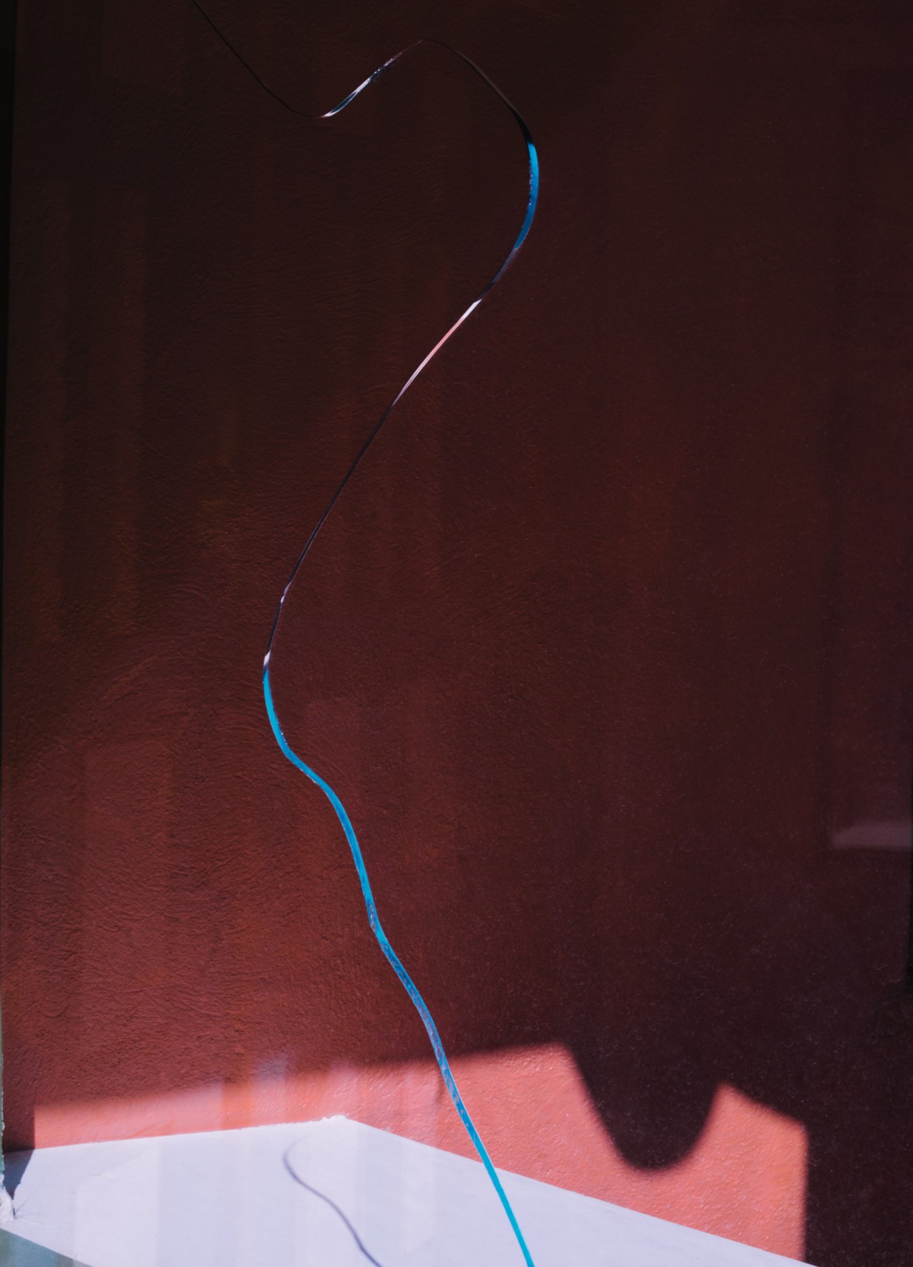 A window with a single crack in it reveals a red painted room on the other side.