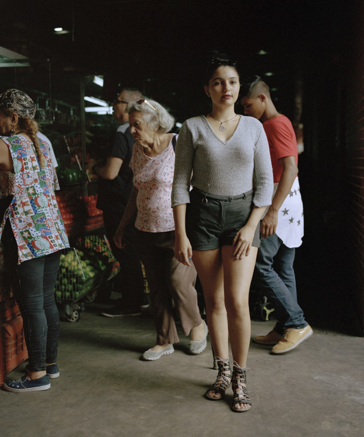 A woman from Venezuela stands in front of other people shopping at farmers market.