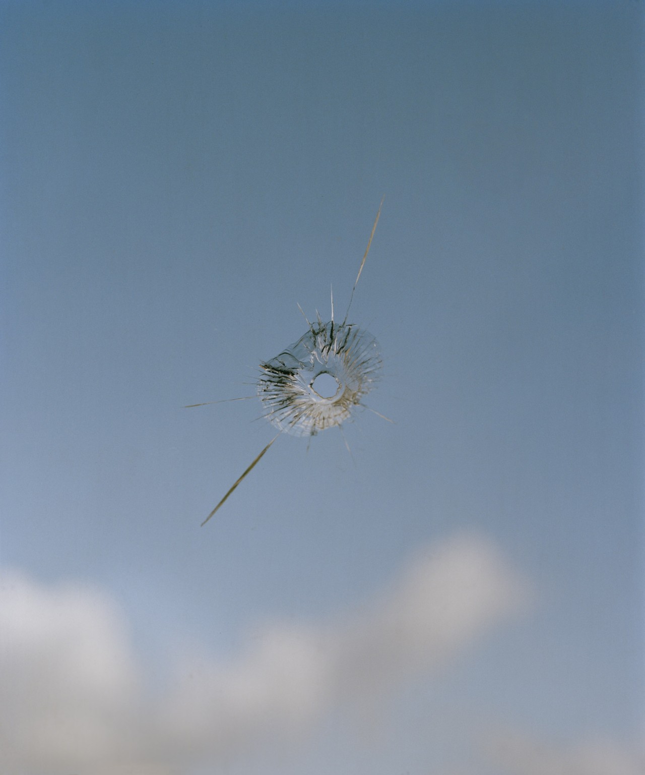 A small hole has pierced a glass window which shows a partially cloudy, blue sky in the background in Venezuela.