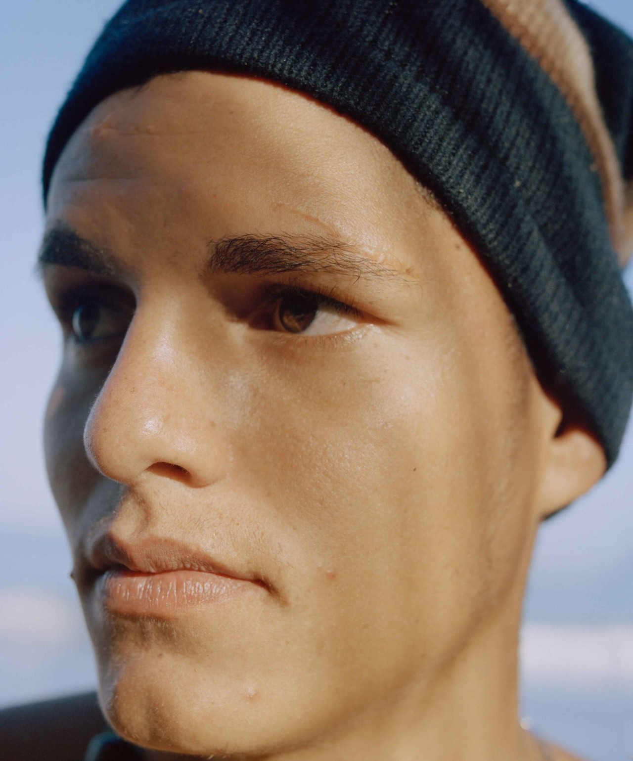 A portrait of a young man from Venezuela wearing a beanie looking into the distance.