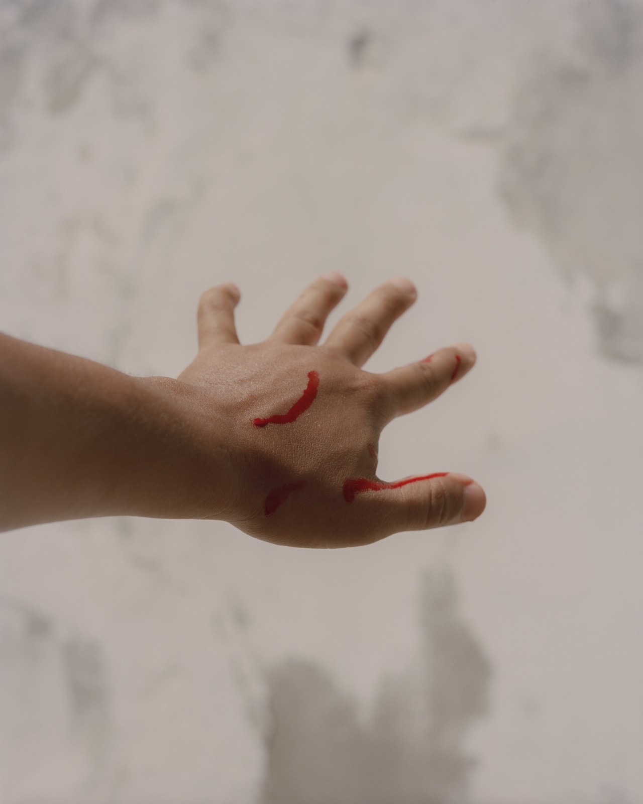 A hand with stretched out fingers has three lines of blood on it.