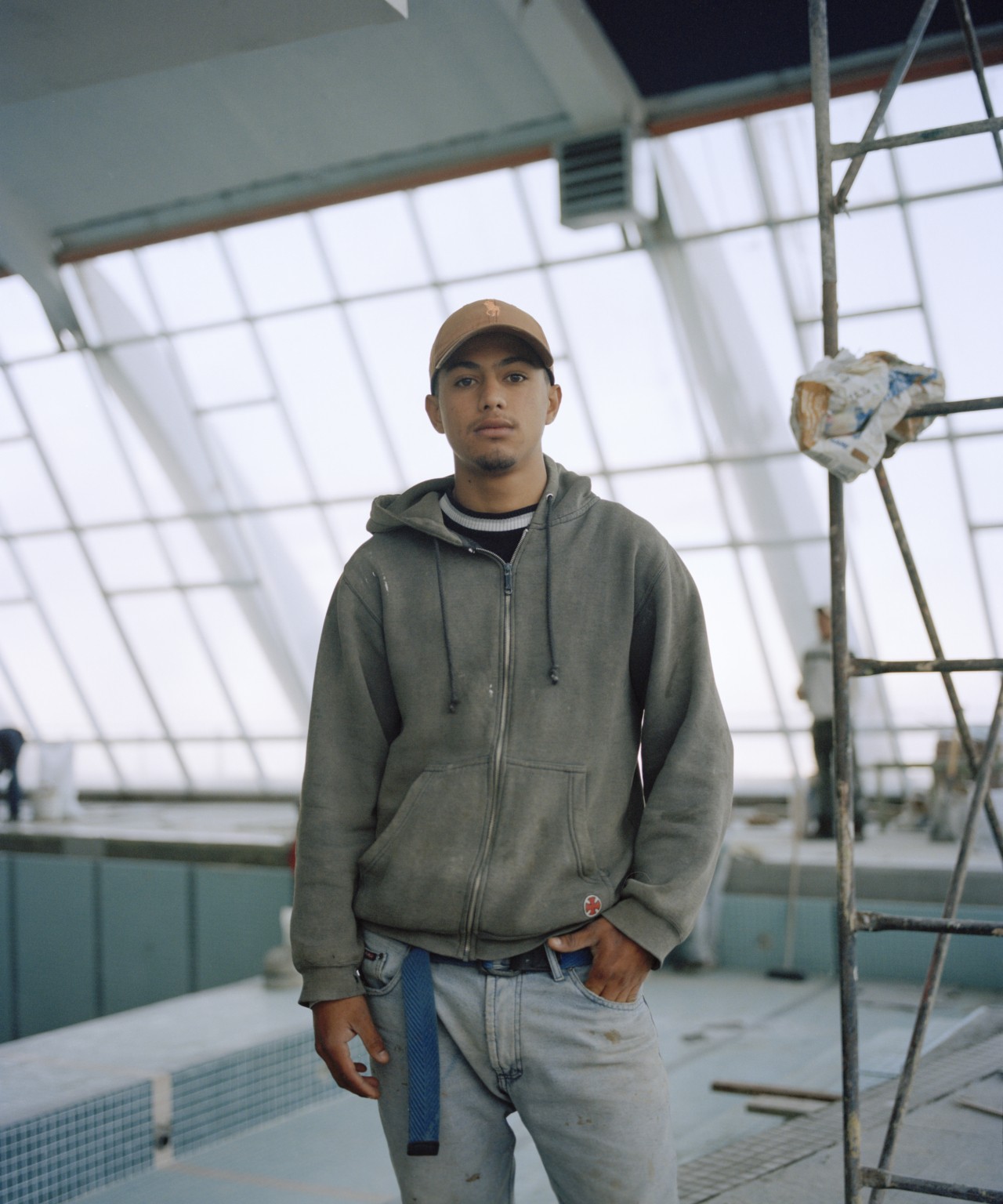 A young man from Venezuela stands in front of an empty pool and construction.