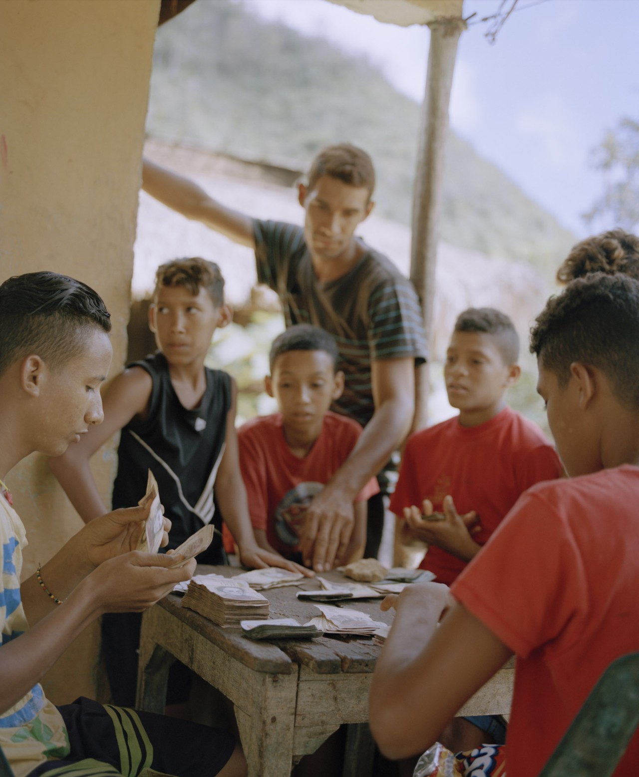 Several Venezuelan youth are sitting around a table counting money.