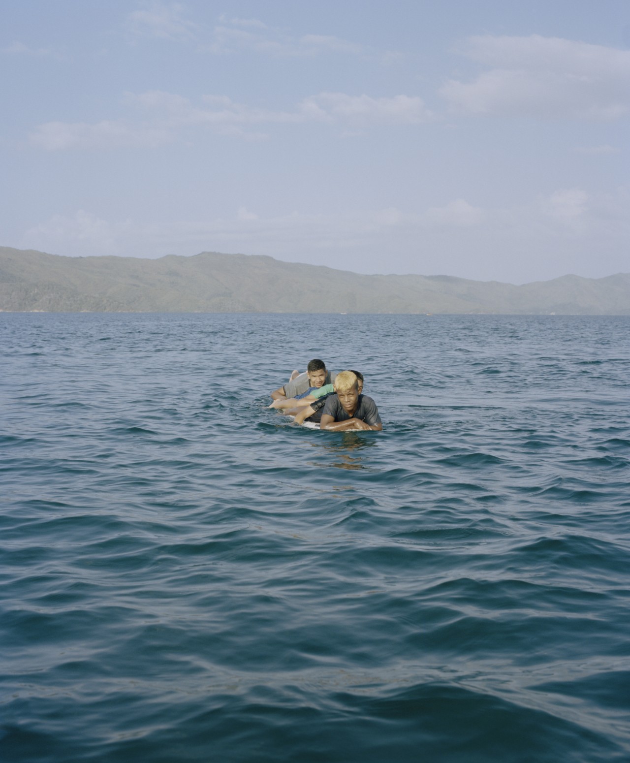 A few Venezuelan youth are lying down on a surfboard in the middle of the ocean.