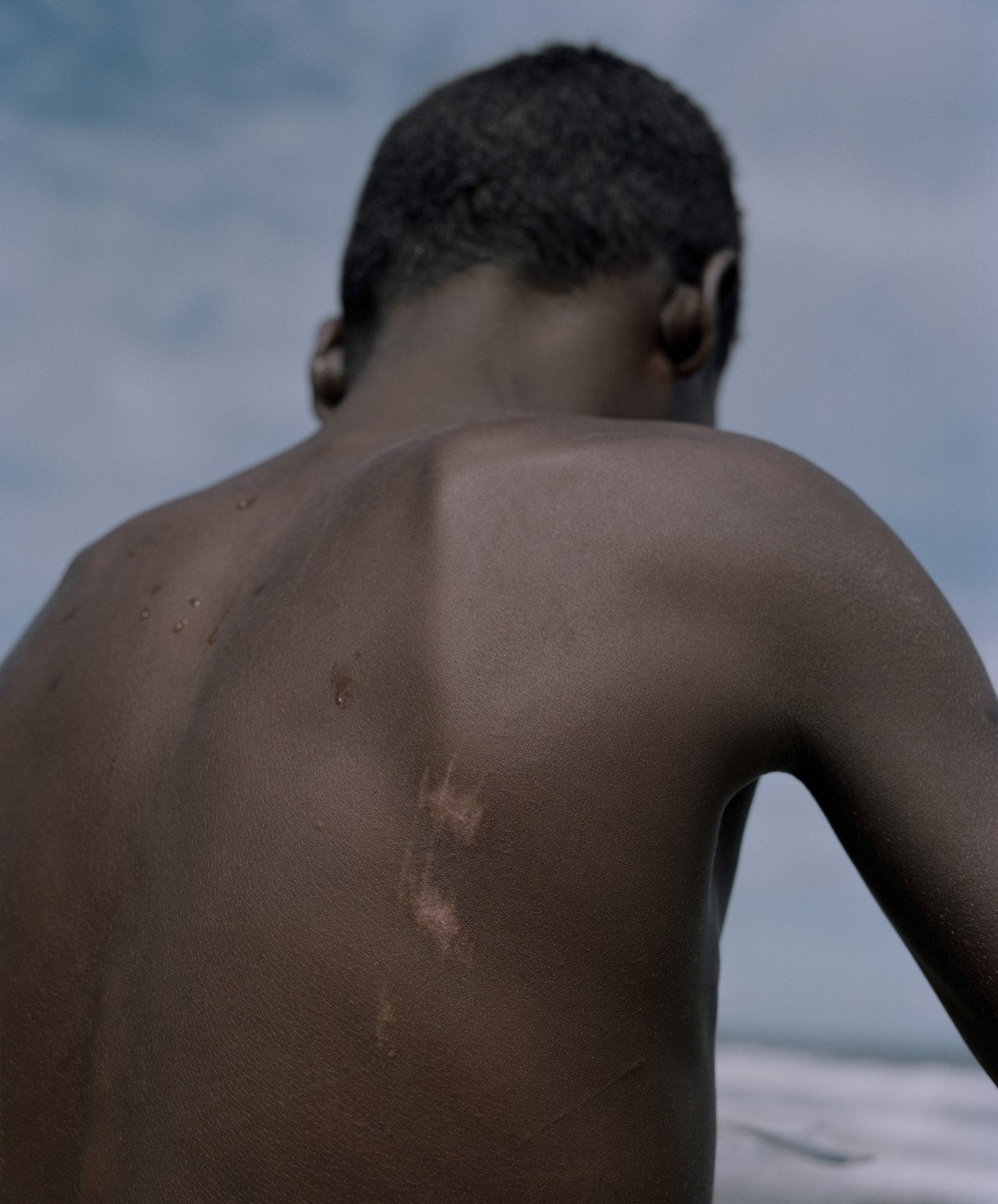 The back of a boy from Venezuela is shown at a beach.