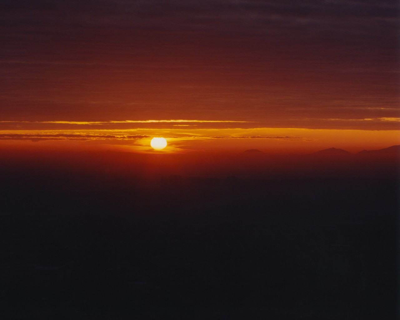 The sun sets in the distance along the hazy orange horizon.